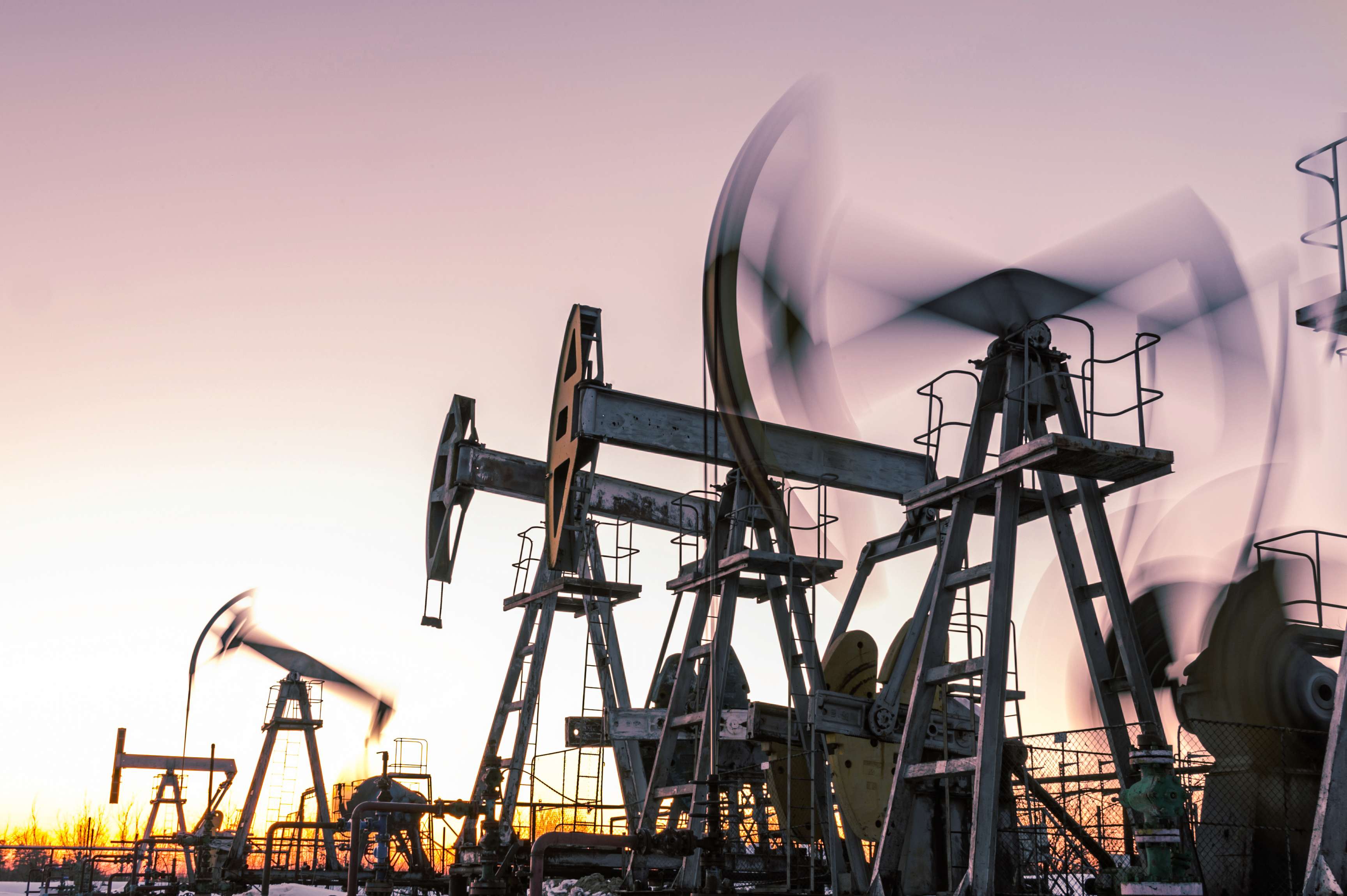 An oil pump drill for oil and gas production is shown in sunset or sunrise.
